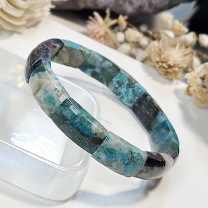 May include: A bracelet composed of rectangular polished stone segments in shades of teal, turquoise, deep blue, and white. The stones feature natural marbling and inclusions, creating a varied pattern throughout the circular band.