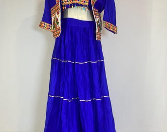 May include: A vibrant blue three-piece outfit featuring a cropped top, a short jacket, and a tiered skirt. The white cropped top is adorned with colorful embroidered birds. The jacket and skirt are a solid blue with gold trim.