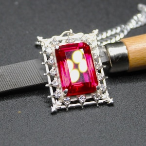 May include: A silver pendant necklace with a large red gemstone set in a silver frame with smaller clear gemstones around the perimeter.