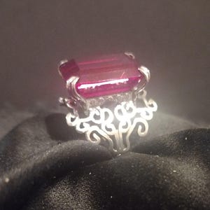 May include: A silver ring with a large, rectangular, dark red gemstone set in a filigree design.