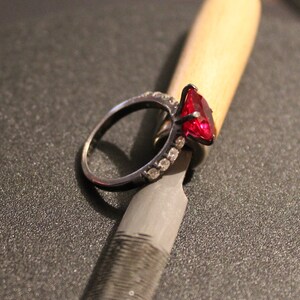 May include: A black ring with a large red gemstone and smaller clear gemstones set in the band.