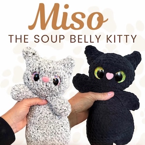 Pu&ograve; includere: Due peluche a forma di gatto, uno in filato grigio e bianco maculato e uno in filato nero tinta unita. Entrambi hanno grandi occhi verdi iridescenti e un piccolo naso rosa. Il testo recita Miso THE SOUP BELLY KITTY e TESTER CALL in bianco e marrone.