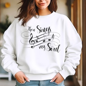 May include: White sweatshirt with black text and musical notes that reads "Then Sings My Soul".