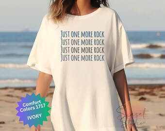 Puede incluir: Una camiseta blanca con el texto "JUST ONE MORE ROCK" repetido cuatro veces en azul.