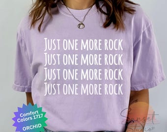 Puede incluir: Una camiseta lavanda con el texto "Just One More Rock" repetido cuatro veces en blanco.