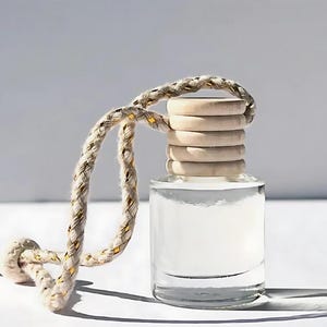 May include: A clear glass bottle with a wooden lid and a beige rope attached. The bottle is filled with a clear liquid and is designed to be hung in a car.