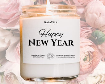 May include: A white candle with a black label that reads "KASAVELA Happy NEW YEAR FREE FROM TOXINS 100% SOY WAX HANDPOURED IN FLORIDA www.SHOPKASAVELA.COM". The candle is surrounded by pink flowers.