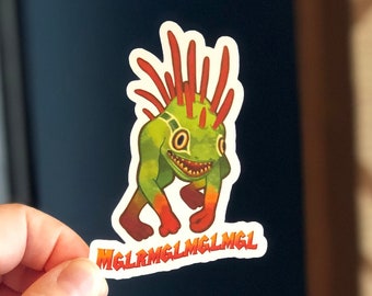 Peut inclure: Un autocollant représentant une créature de dessin animé avec un corps vert, des épines rouges et des jambes orange. La créature a un large sourire et le texte "MGLMGLMGLMGL" est imprimé en dessous. L'autocollant est tenu sur un fond bleu foncé.