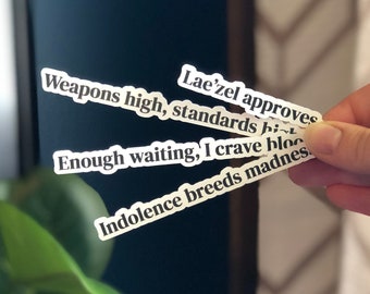 Peut inclure: Un ensemble de quatre autocollants en papier blanc avec du texte noir. Le texte sur les autocollants est : "Weapons high, standards high", "Lae'zel approves", "Enough waiting, I crave blood", et "Indolence breeds madness".