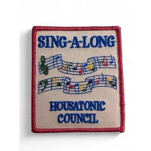 Puede incluir: Un parche bordado rectangular con fondo beige y borde rojo. Presenta el texto azul SING-A-LONG y HOUSATONIC COUNCIL, con dos pentagramas musicales azules que contienen notas musicales bordadas de colores entre el texto.