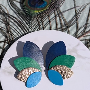 Pode incluir: Um par de brincos com segmentos sobrepostos em forma de pétala nas cores azul-marinho, verde-floresta, dourado metálico e azul brilhante. Cada brinco é composto por várias peças curvas dispostas em leque, criando uma aparência texturizada com acabamentos lisos e granulados.