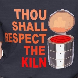 May include: Navy blue t-shirt with the text "THOU SHALL RESPECT THE KILN" in orange and red. A cartoon kiln illustration is on the right. The kiln is open, revealing a red interior.