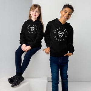 Op de afbeelding: Twee kinderen dragen zwarte hoodies met de tekst "BEEF LOVER'S CLUB" in een cirkelvormig ontwerp rond een koeienafbeelding. De hoodies hebben een voorzak en een capuchon met trekkoord. Het ene kind draagt een donkerblauwe spijkerbroek, het andere een blauwe spijkerbroek.