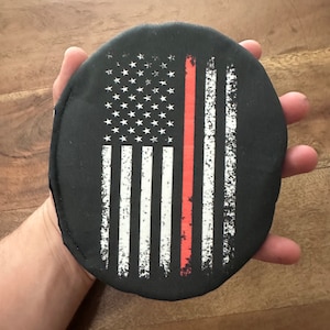May include: A black round disc with a white and red American flag design. The flag has a thin red line down the center of the stripes.