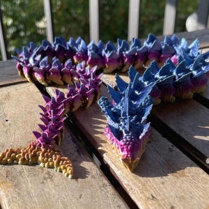 Könnte beinhalten: Eine 3D-gedruckte, segmentierte, lila und blaue, stachelige, drachenartige Kreatur mit einem Schwanz. Die Kreatur ist aus Kunststoff und hat eine strukturierte Oberfläche.