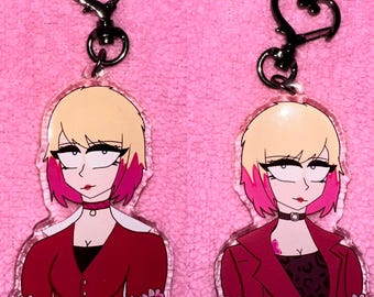 May include: Two clear acrylic keychains featuring a cartoon illustration of a woman with blonde hair and pink highlights. She is wearing a red jacket, a black choker, and a black top. The keychains are decorated with a border of pink flowers.