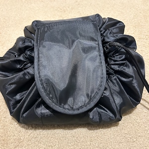 May include: Black drawstring makeup bag with a zipped pocket on the front.