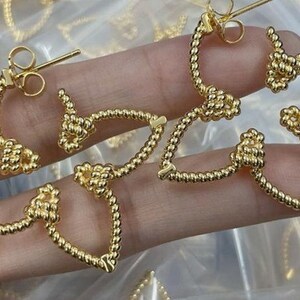 May include: A pair of gold-toned hoop earrings with a knotted design. The earrings are made of a twisted rope-like material.