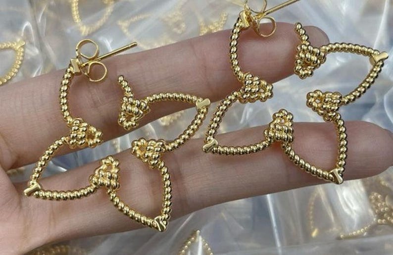 May include: A pair of gold-toned hoop earrings with a knotted design. The earrings are made of a twisted rope-like material.