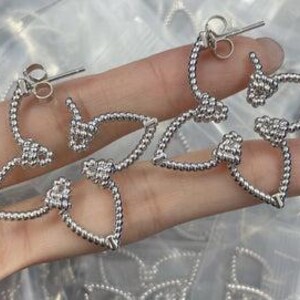 May include: A pair of silver earrings with a delicate, twisted design. The earrings are shaped like a teardrop with a small ball at the end.
