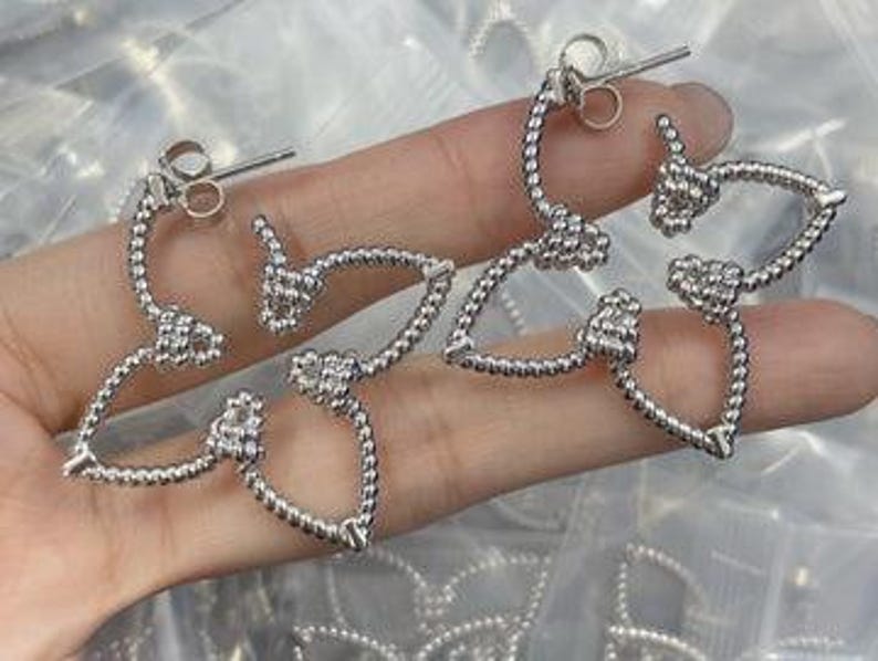 May include: A pair of silver earrings with a delicate, twisted design. The earrings are shaped like a teardrop with a small ball at the end.
