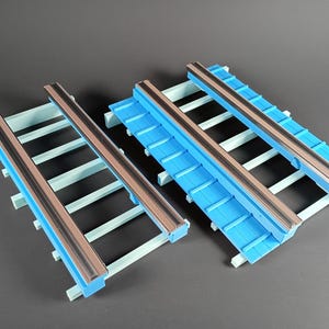 May include: Two blue and white toy train tracks with brown rails. The tracks are made of plastic and are designed to connect together. The tracks are set against a gray background.