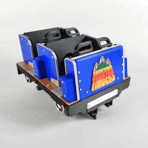 May include: A blue and black miniature roller coaster car with the words "SHIVERING TIMBERS" printed on the side. The car has two seats and a wooden base.