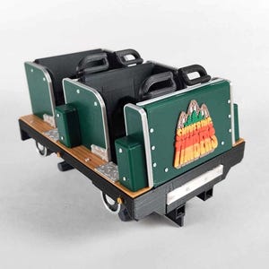 May include: A miniature roller coaster car with two rows of seats. The car is primarily green, black, and brown, with the words "Shivering Timbers" and a mountain graphic on the back. The car has black handles and wheels.
