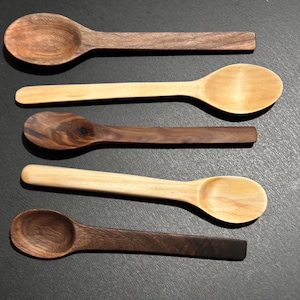 Può includere: Cinque cucchiai di legno, due di colore marrone scuro e tre di colore marrone chiaro, disposti in fila su una superficie nera.