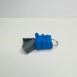 Op de afbeelding: Een blauwe siliconen sleutelhanger in de vorm van een beer met een zilveren ring. De sleutelhanger is open en de binnenkant is grijs.