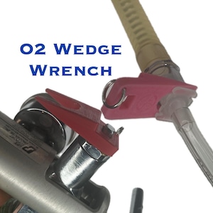 May include: A red and pink plastic O2 Wedge Wrench tool for loosening and tightening oxygen tank valves. The wrench is designed to fit over the valve and has a handle for leverage. The text "O2 WEDGE WRENCH" is visible in the image.