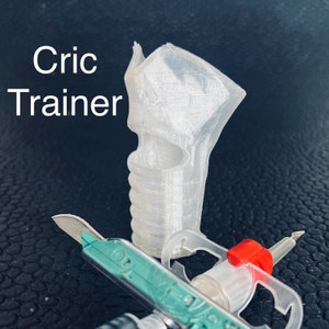 Könnte beinhalten: Ein weißer Cricket-Trainingshilfe aus Kunststoff mit einer strukturierten Oberfläche. Die Hilfe ist in Form eines Cricket-Schlägers geformt und hat ein Loch oben. Die Hilfe liegt auf einer schwarzen Oberfläche.