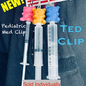 Op de afbeelding: Drie kleurrijke gummy bear-vormige spuitbeugels met een heldere spuit die aan elk is bevestigd. De spuiten zijn gemarkeerd met milliliter-markeringen. De tekst "TED CLIP" is geschreven in blauwe letters op een zwarte achtergrond. De tekst "Pediatric Med Clip" is geschreven in zwarte letters op een witte achtergrond. De tekst "Sold Individually" is geschreven in rode letters op een grijze achtergrond.