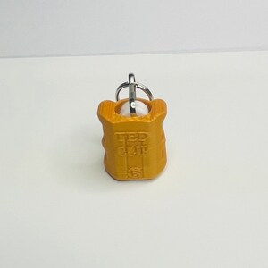 Op de afbeelding: Een goudkleurige sleutelhanger met een metalen ring en de woorden "LED CLIP" erop gegraveerd.