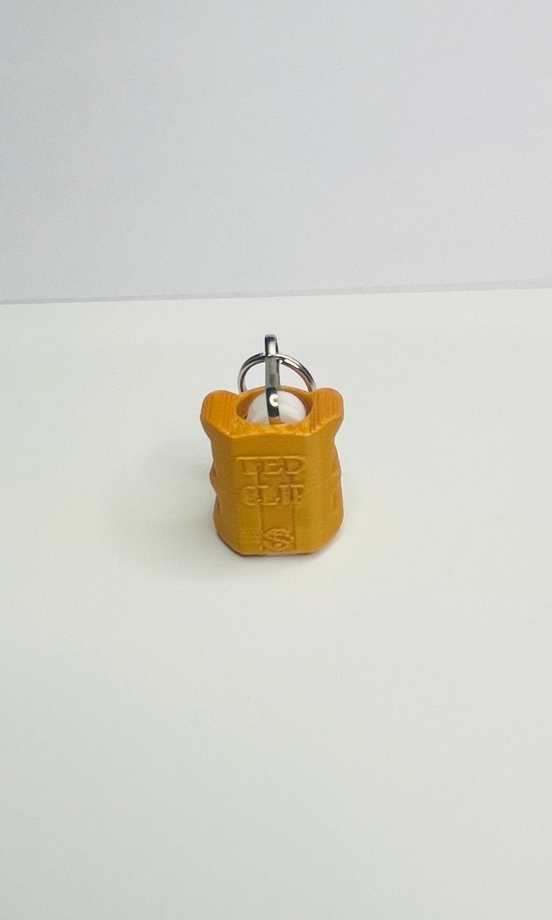 Op de afbeelding: Een goudkleurige sleutelhanger met een metalen ring en de woorden "LED CLIP" erop gegraveerd.