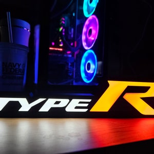 May include: An illuminated sign with the text "TYPE R" in white and orange. The sign is on a wooden surface.