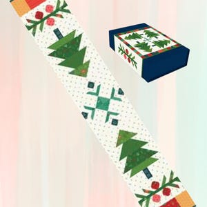 May include: A white table runner with a repeating pattern of green Christmas trees, red berries, and snowflakes. The runner is bordered with red, green, and yellow fabric. A matching box is also shown.
