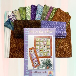 May include: A collection of fabric squares in various shades of green, brown, purple, and blue, with a white fabric square in the background. The fabric squares are arranged in a fan shape. A printed pattern for a quilt titled "We're On A Roll" is in the center of the image. The pattern features a quilt design with a variety of colorful squares and a design of toilet paper rolls. The pattern is from Java House Quilts.