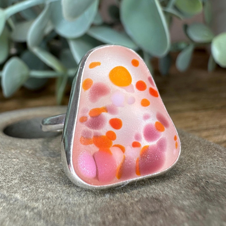 May include: A silver ring with a pink, orange, and white glass stone. The stone has a speckled pattern.