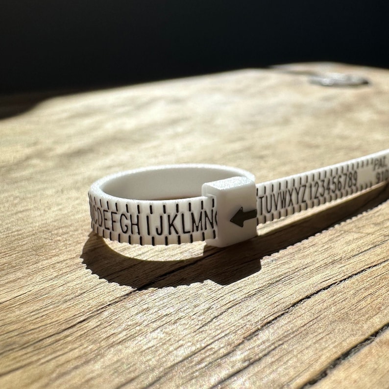 May include: White plastic ring sizer with black markings. The sizer has letters A through Z and numbers 1 through 9 printed on it.