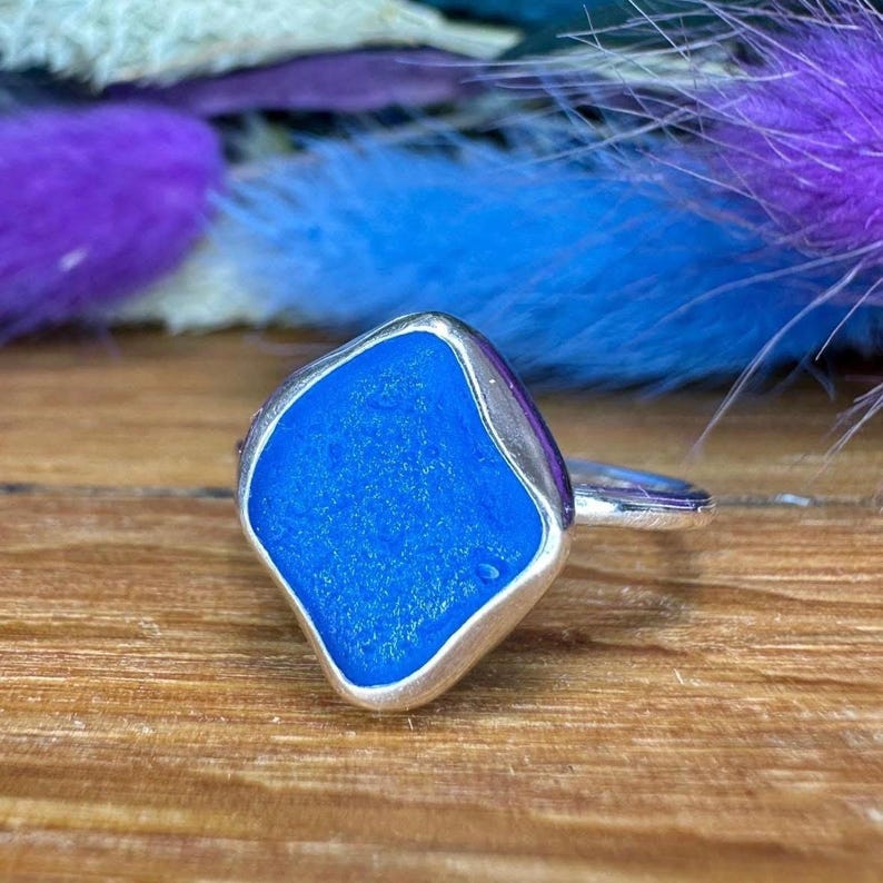 May include: A silver ring with a square blue glass stone set in the center.