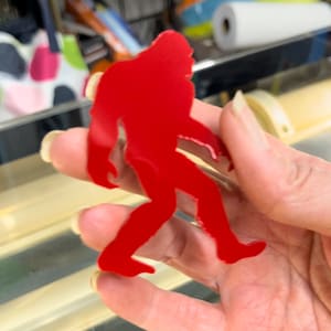 May include: A red silhouette of a Bigfoot walking, cut out of metal.