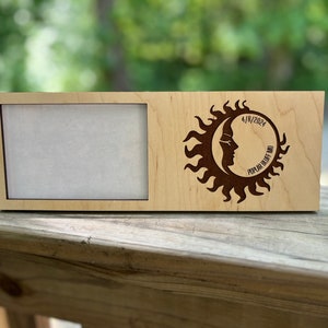 May include: A wooden picture frame with a cutout of a sun and moon design. The design includes the text "4/18/2024 Poplar Bluff MO".