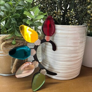 May include: A black ear cuff with five colorful light bulb charms. The charms are red, yellow, teal, pink, and green.