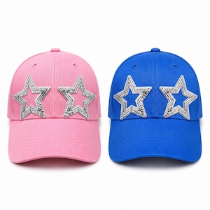 Puede incluir: Dos gorras de béisbol, una de color rosa claro y otra de color azul real, cada una con dos estrellas de lentejuelas plateadas en los paneles frontales. Ambas gorras tienen una corona estructurada, una visera curva y botones superiores a juego.