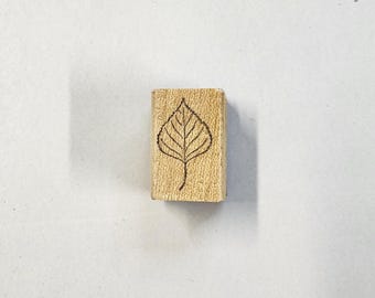 May include: A wooden stamp with a leaf design. The leaf is outlined in black and has a detailed vein pattern.