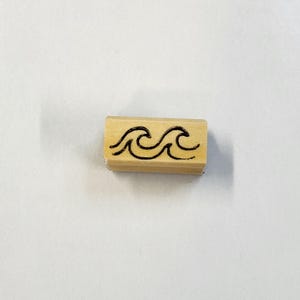 May include: A wooden stamp with a black ink design of two waves.