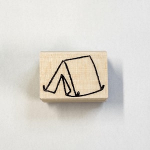 May include: A wooden stamp featuring a simple line drawing of a tent.