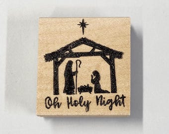 May include: A wooden rubber stamp with a silhouette of the nativity scene and the text "Oh Holy Night".