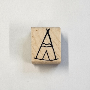 May include: A wooden stamp with a black line drawing of a teepee tent with a flap open. The teepee has a decorative band around the middle.